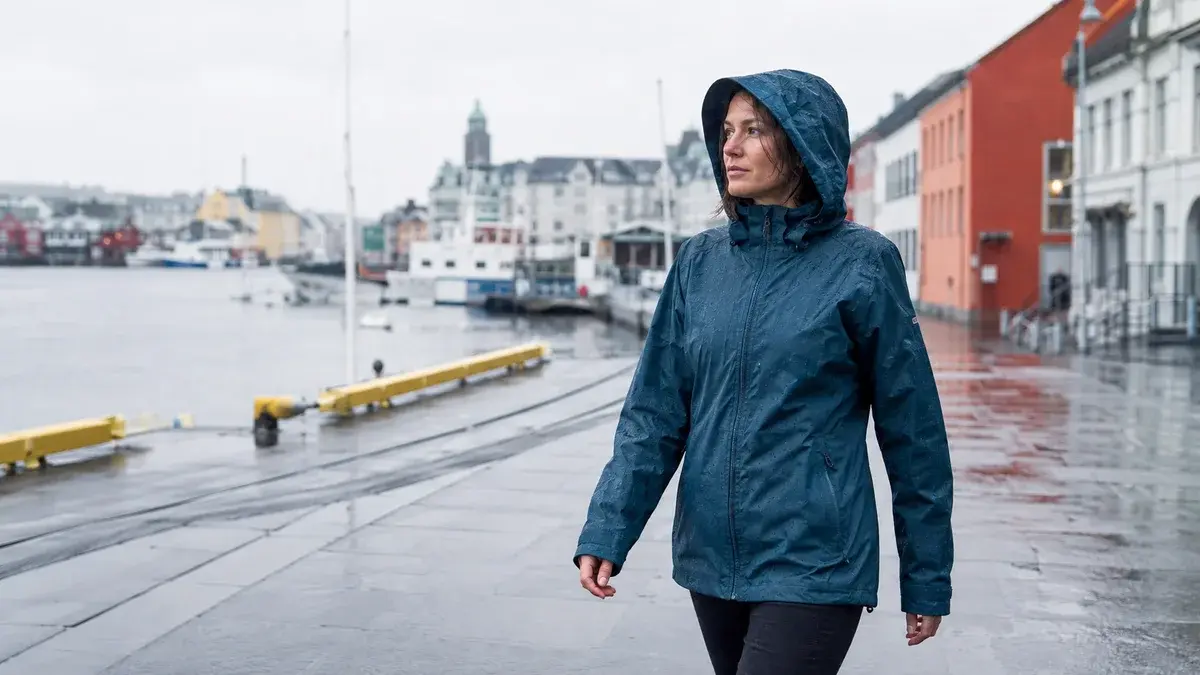 Kvinne i blå regnjakke på en regnvåt norsk havnepromenade